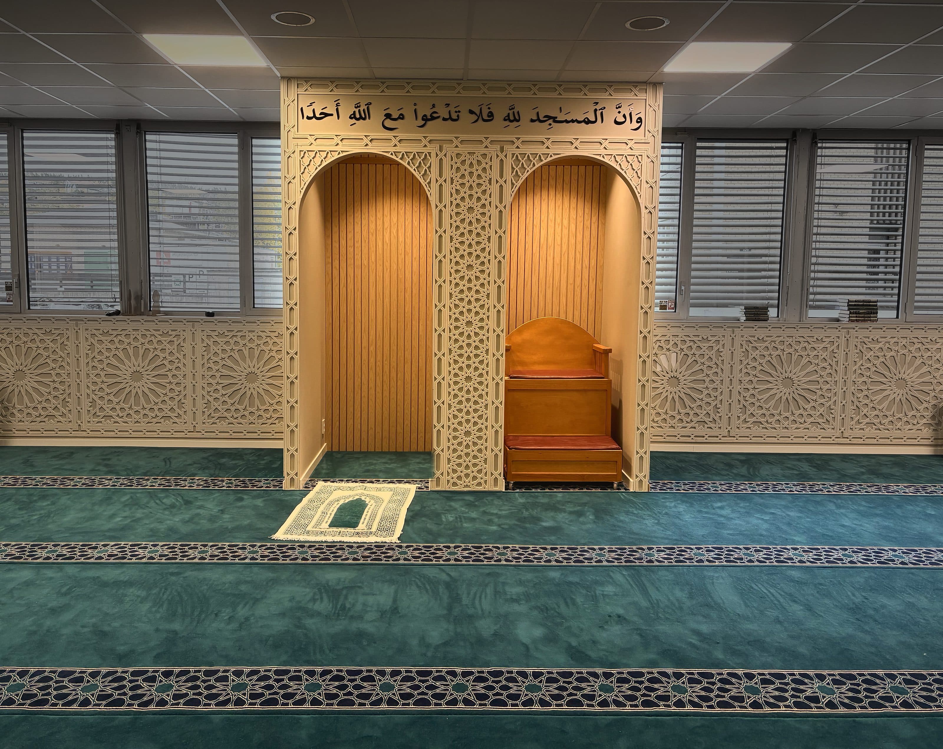 Mihraben og minbaren i Masjid Rahma, under verset fra Koranen 72:18, med bønneteppet foran.